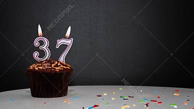 Muffin on black with a number from a candle number 37. Copy space, a pie on a black background, a card for congratulations on your