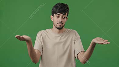 Puzzled man confused uncertain hispanic arab thoughtful young guy standing in green studio shrugs shoulders make choice