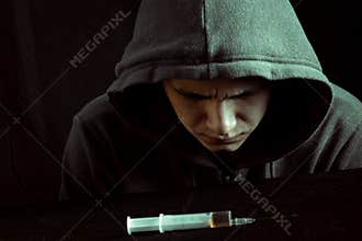 Grunge image of a depressed drug addict looking at a syringe and drugs
