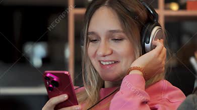 A pretty woman sings along listening to loud music at home. young girl is sitting on couch and listening to music with