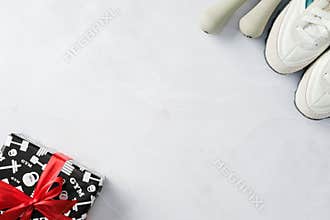 Fitness-themed gift box with red ribbon, white sneakers, and dumbbells on a marble surface.