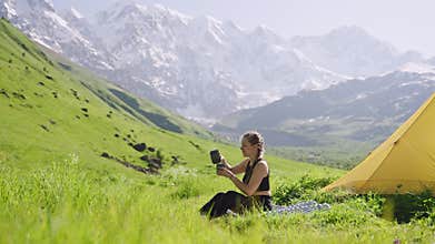 Woman on backpacking trip cooks with portable mini gas stove outdoors. She boils water in a pot, makes tea, then turns