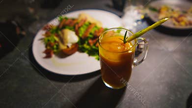 Glass of iced tea with straw, next to a plate of food on a dark table