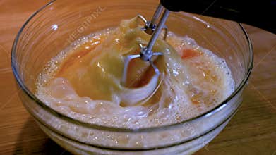Electric mixer whipping eggs into airy foam in glass bowl, ideal for dessert, cake batter or cream preparation. Closeup of frothy