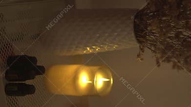 A candle lights a dim room, revealing shadows of dried flowers