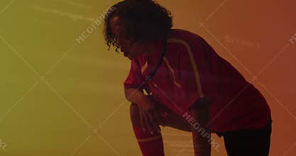 Crouching in red sports uniform, person against vibrant orange and yellow background