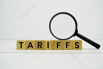 TARIFFS alphabet letters with magnifying glass on wooden background