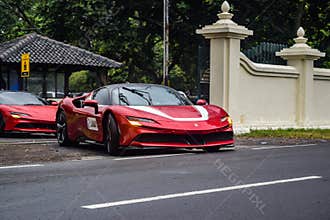 Red Ferrari SF90 stradale Plug-in Hybrid Electric Vehicle PHEV hypercar driving on the wet road after rain