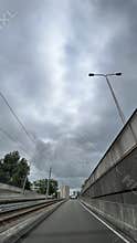 Stormy urban roadway beside tram tracks and concrete sound walls, viewed from