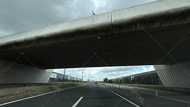 Motorway passing beneath stained concrete overpass beside modern industrial