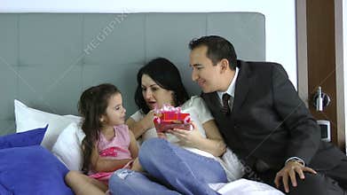 Husband giving a gift to his wife with daughter on the bedroom