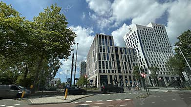 Modern office towers beside busy city intersection with trees, cars, cyclists