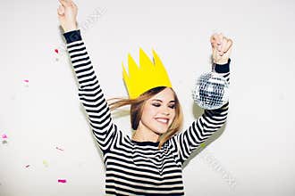 Young smiling woman on white background celebrating party, wearing stripped dress and yellow paper crown, happy dynamic