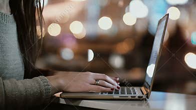 Close-up view of female hands typing on laptop computer. Young woman sitting near the window in evening and use wi-fi.