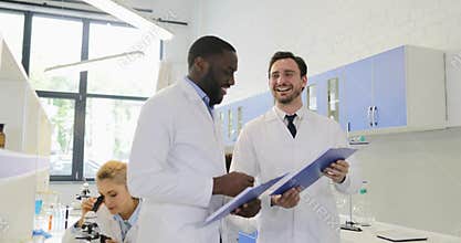 Two scientists holding documents with experiment results talking happy smiling and shaking hands cheering of success in