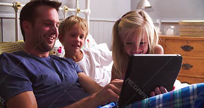 Father With Children Looking At Digital Tablet In Bed