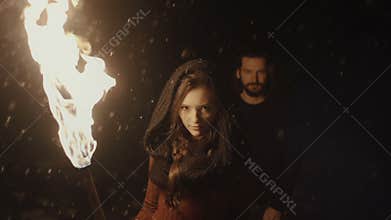 Portrait of a young mystic couple holding a torch in the dark forest.