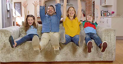 Family waving at camera on couch