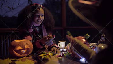 Cute black girl in devil mask frightening her friend on Halloween night