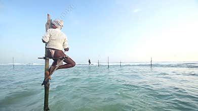 GALLE, SRI LANKA - MARCH 2014: Old fisherman on a fishing pole in the ocean in Galle. Stilt fishing is a tradition that only about