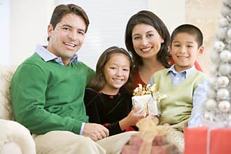 Family Sitting On Sofa Holding A Christmas Gift