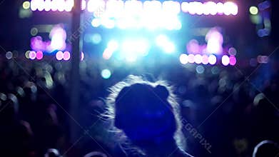 Young girl having fun dancing at a rock concert on the background of the scene with colored lights