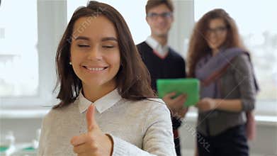 Smiling girl gestures good quality in front of man and woman with tablet