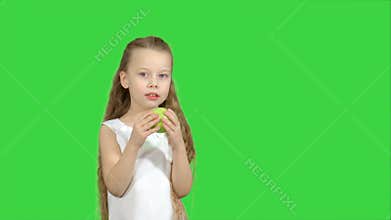 Portrait of a little girl eating green apple on a green screen, chroma key