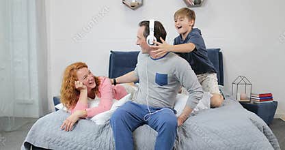 Happy Family Using New Headphones Listening To Music In Bedroom Spending Time Together In Morning