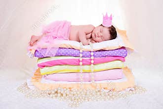 Newborn baby girl in a crown sleeping on the bed of mattresses. Fairy Princess and the Pea