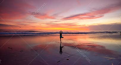 A lone woman doing yoga on a beach at sunset