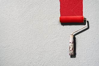 Paint roller painting with red paint on white wall