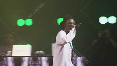 Mc african man performing on stage on party in nightclub. Green spotlights.
