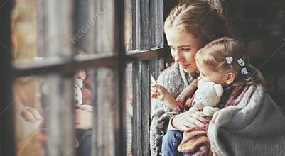 Family mother and child daughter look out window on rainy autumn