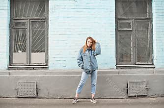 Portrait of a stylish girl at full height against a background of blue wall in retro windows. The girl poses against the