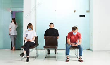 Young people in medical masks, sitting in a queue and waiting for a doctor`s appointment in the hospital.