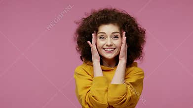 Oh my god, wow! Amazed excited girl afro hairstyle in hoodie raising hands in surprise, looking at camera