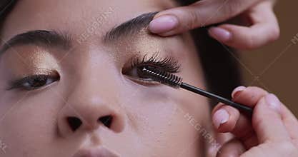 Make up artist applying mascara on female lashes, closeup