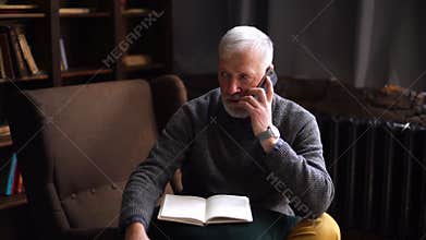 Serious handsome gray-haired mature man talking on cell phone and taking notes in paper documents.