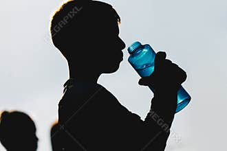 Silhouette of young boy drinking water after outdoor activity