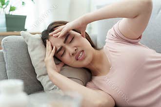Asian woman are holding their hands to the head in pain  sleeping on sofa at home, Young women have severe headaches from