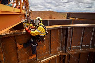 Side view of industrial  rope access welder maintenance abseiler wearing fall safety body safety harness helmet protective