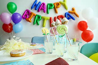 Table with treats and HAPPY BIRTHDAY made of colorful balloon letters in living room