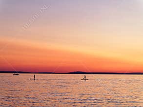 Stand up paddle surfing on lake by twilight glow in sky