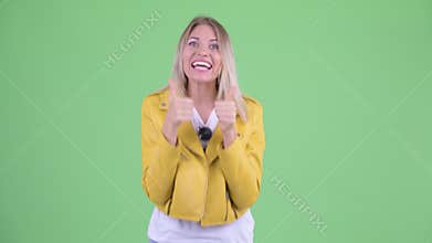 Happy young rebellious blonde woman giving thumbs up and looking excited