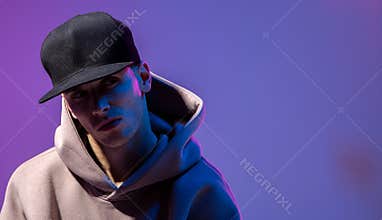 Men portrait in a neon light. Beneath in the hoodie and hat. Dark face. Hip-hop style.