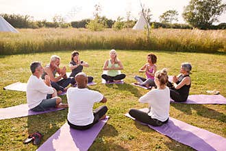 Group Of Mature Men And Women In Class At Outdoor Yoga Retreat Sitting Circle Meditating