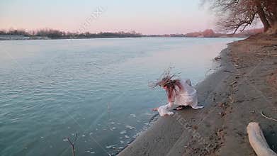 Woman in the image of witch and old Slavic costume runs on Bank of river near forest