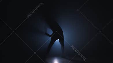 Silhouette of young man warming up before training in dark studio with smoke.
