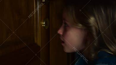 Close-up of a cute charming little girl smiling and peeking through the keyhole